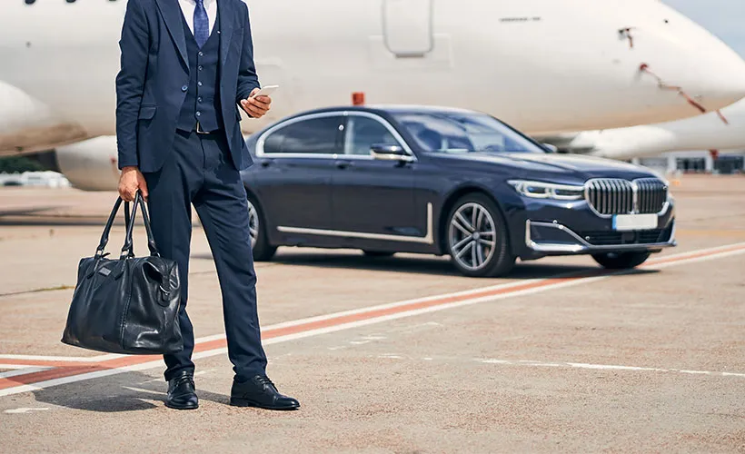 A well-dressed man stands beside a car, exuding professionalism and elegance in his suit and tie.